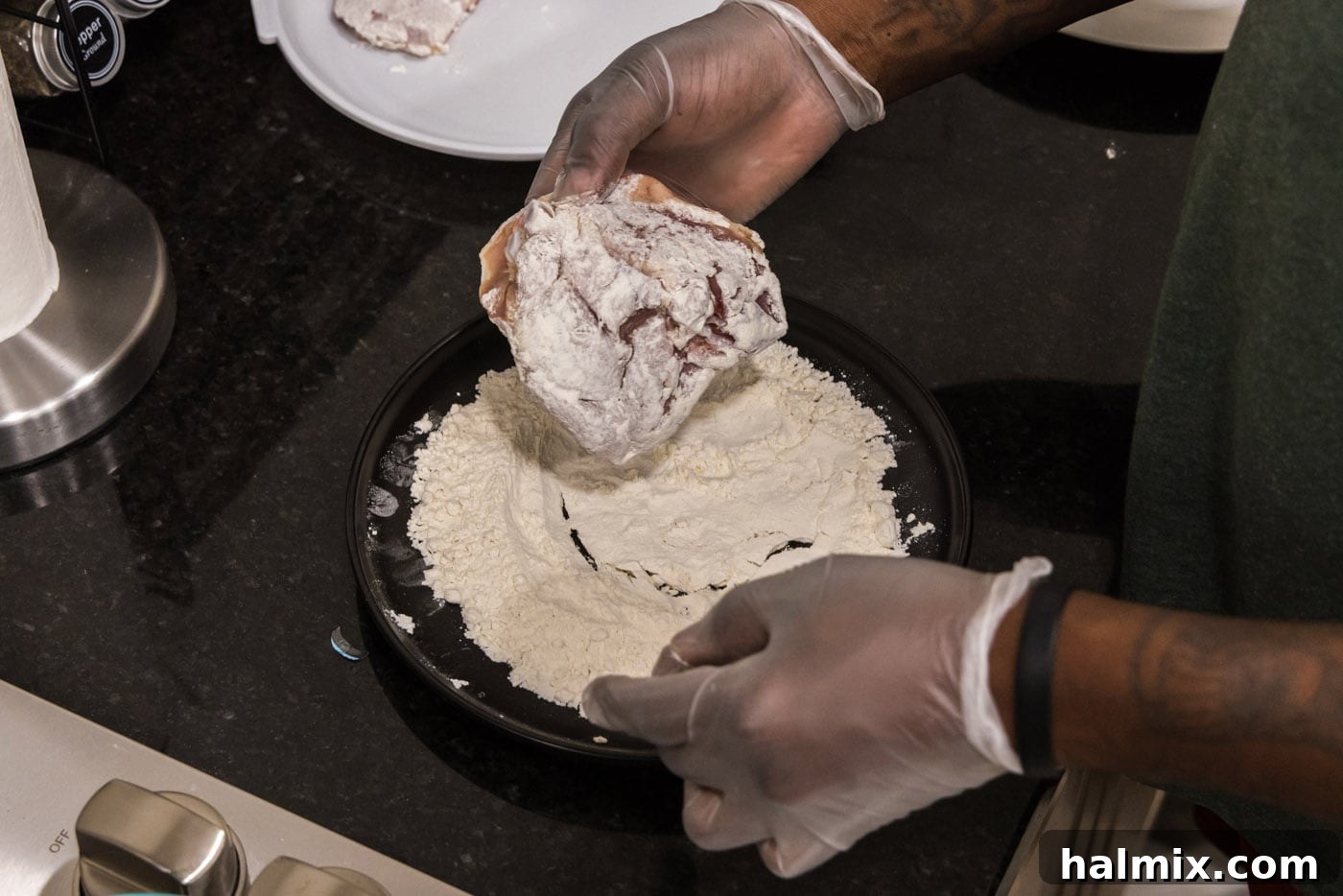 hand dredging chicken thigh in flour