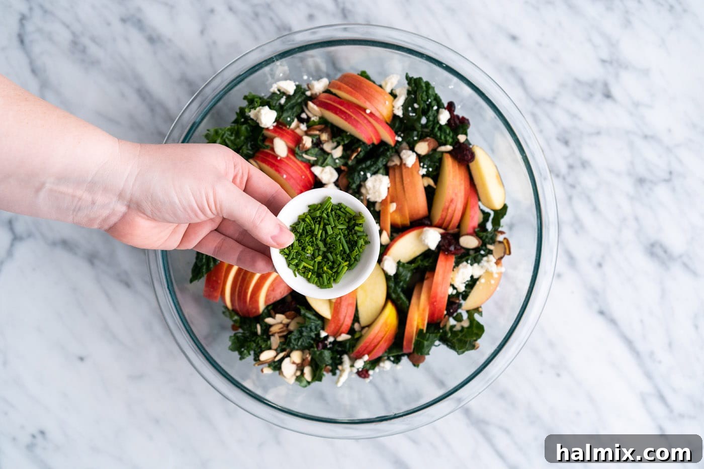 Adding chives to kale salad in a bowl