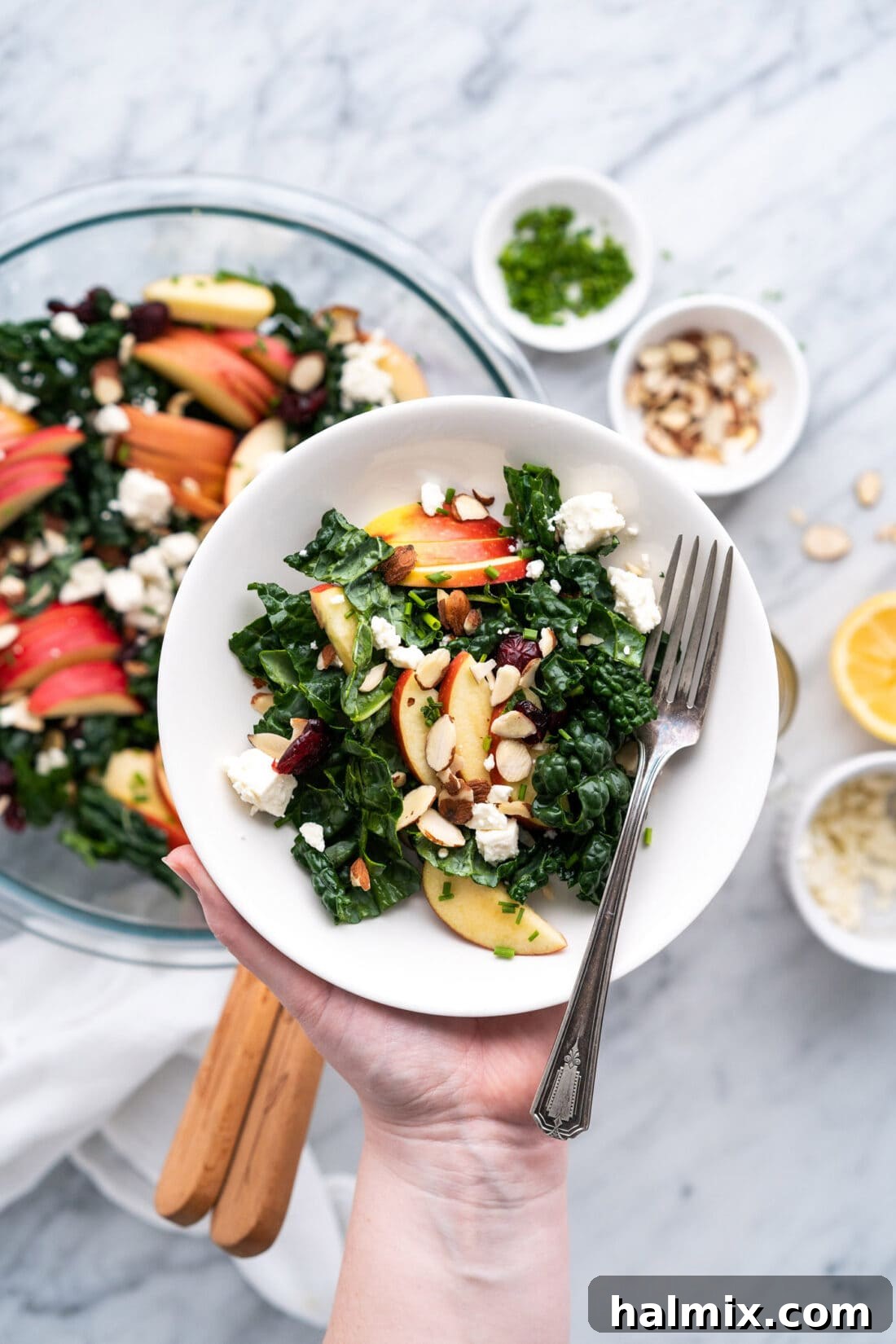 Single serving of Kale Salad in a bowl being held over the batch of Kale Salad