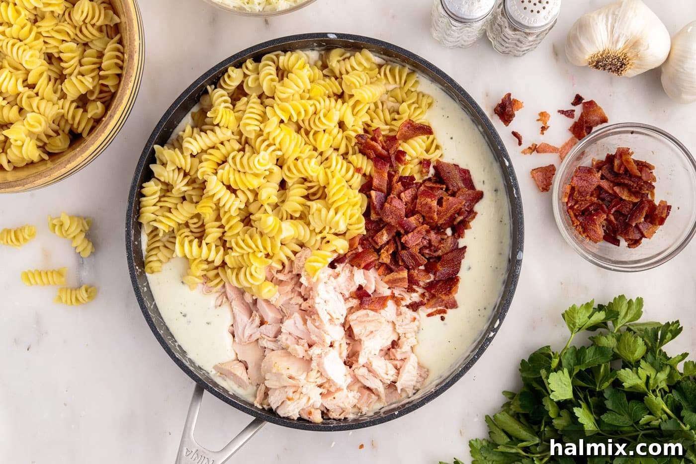 pasta, bacon, and chicken added to cream cheese sauce in a skillet