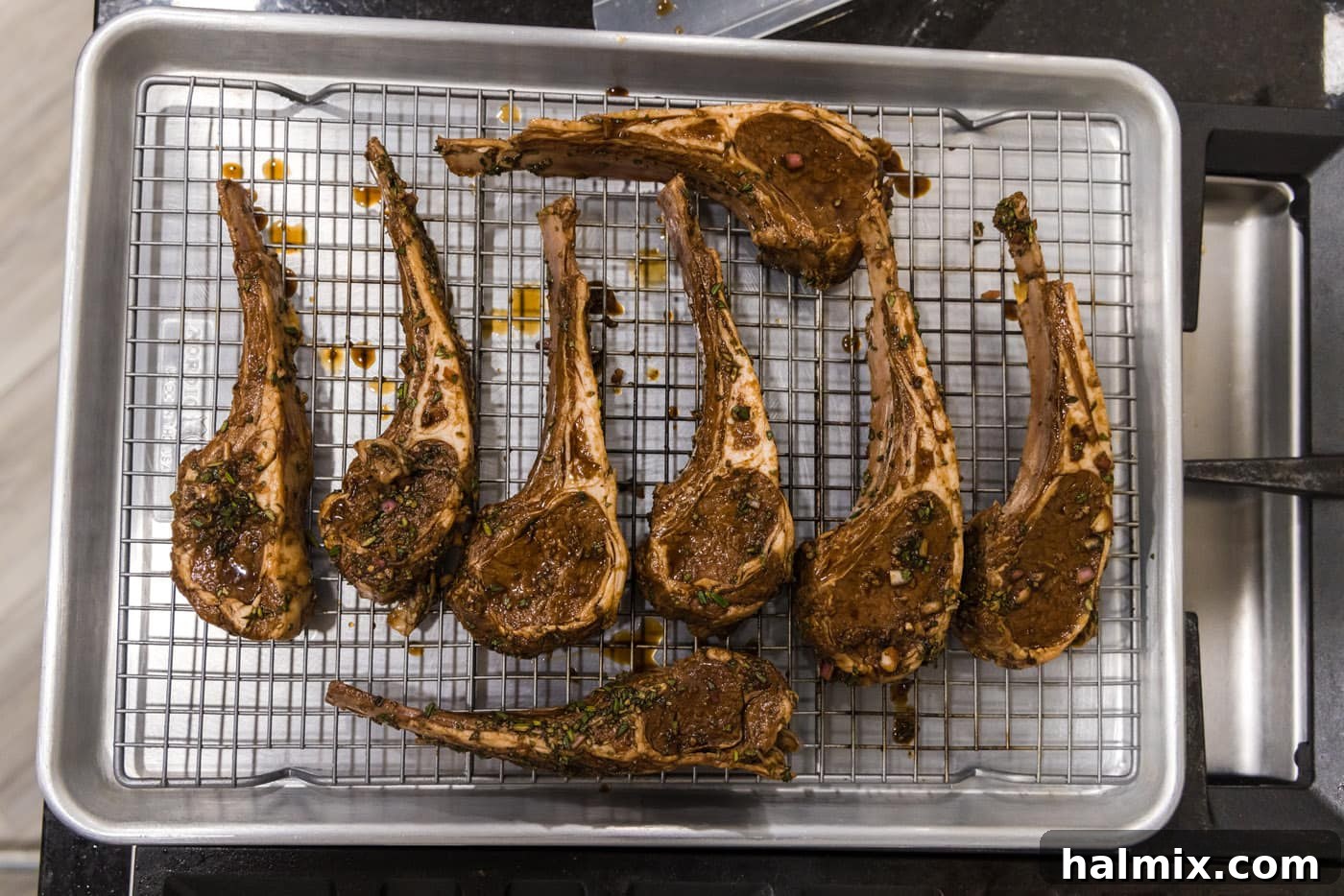 Perfectly seasoned lamb chops resting on a wire rack over a baking sheet, ready for the broiler.