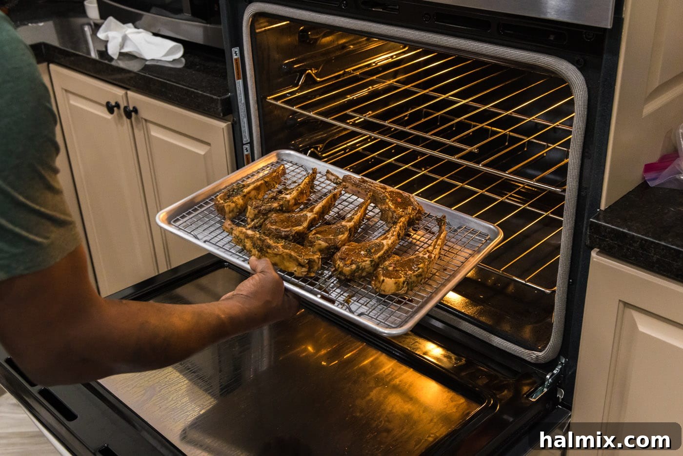 A baking sheet with lamb chops being carefully placed under the broiler in an oven, showing the high heat environment.