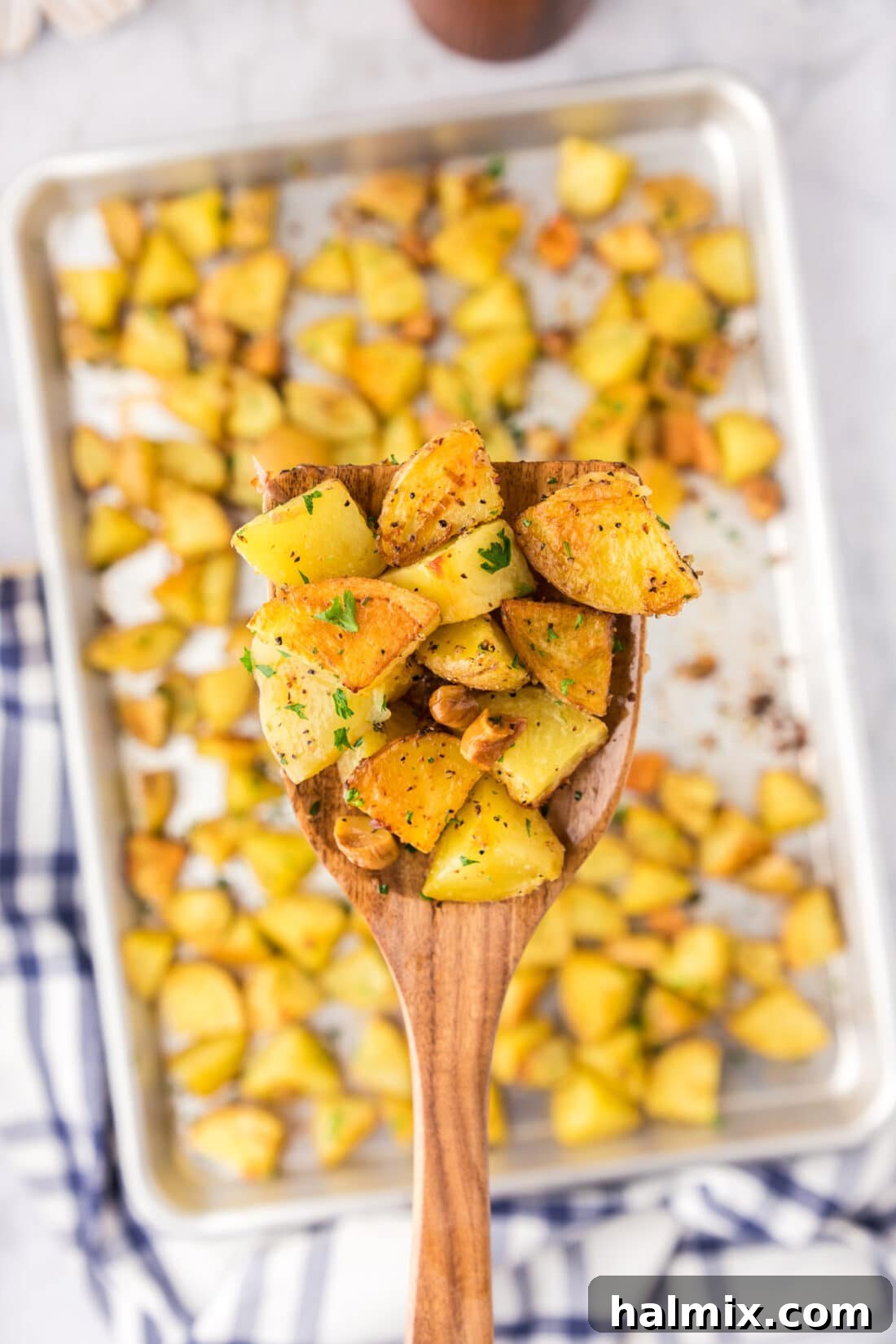 Spatula of Garlic Roasted Potatoes held over a pan of Garlic Roasted Potatoes