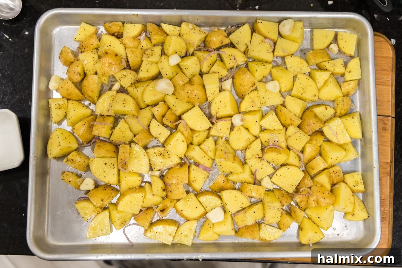 cubed potatoes on a baking sheet with garlic cloves on top