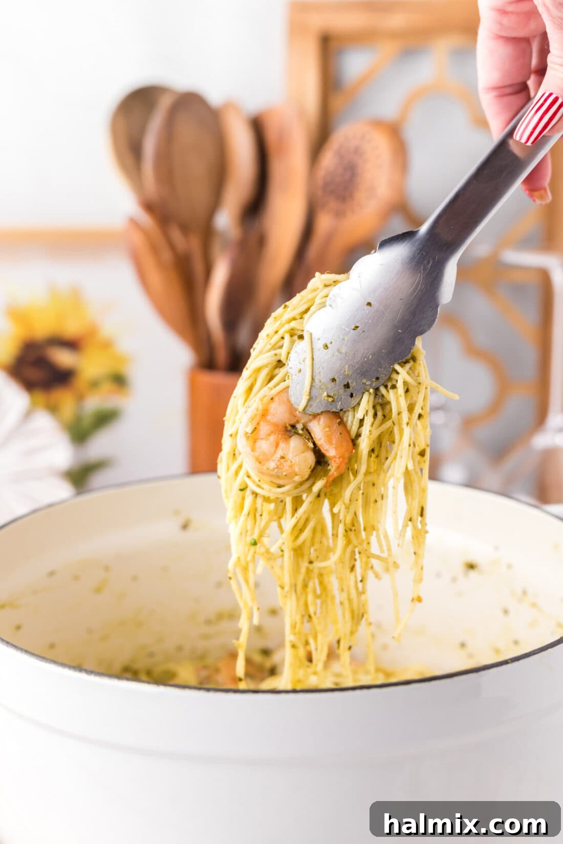 Tongs picking up a portion of delicious Shrimp Pesto Pasta from a serving bowl
