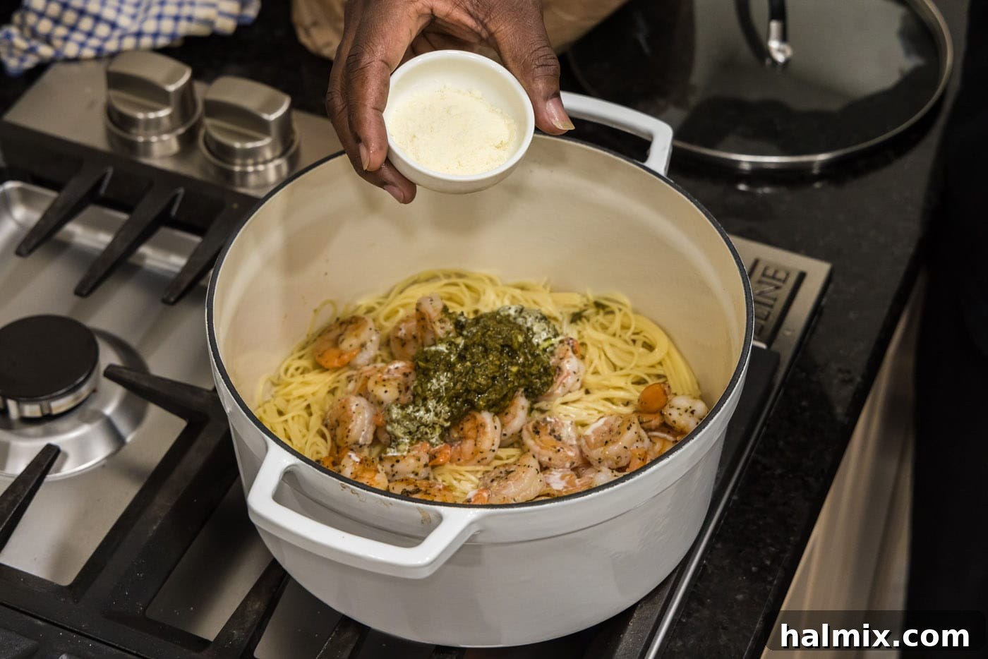 Pouring grated Parmesan cheese into the shrimp pesto pasta pot