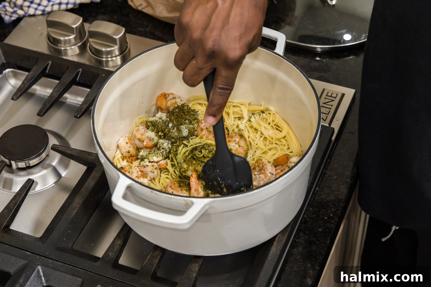 Stirring shrimp pesto pasta thoroughly with a rubber spatula