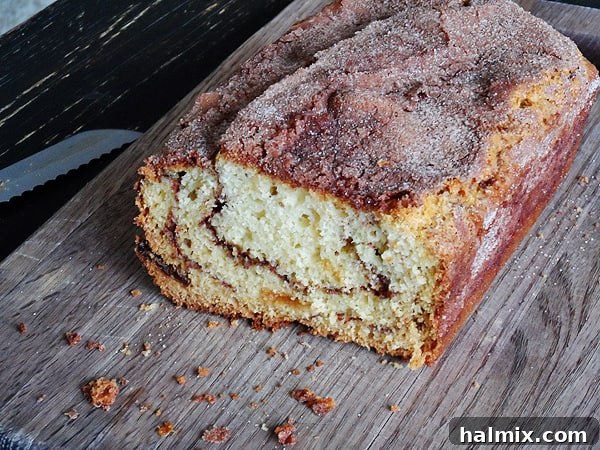 Aromatic Cinnamon Raisin Swirl Loaf 6 A whole loaf of cinnamon raisin swirl quick bread, freshly baked and golden brown, resting on a wooden cutting board.
