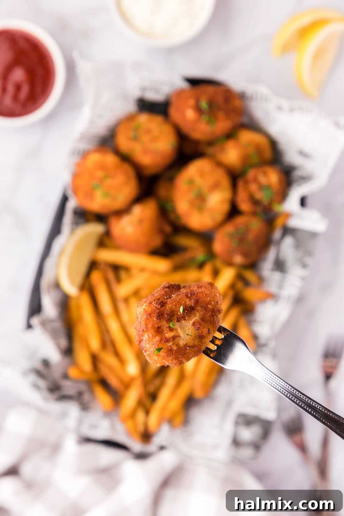 Golden Seared Scallops 15 A Fried Scallop on a seafood fork held above a basket of Fried Scallops and fries
