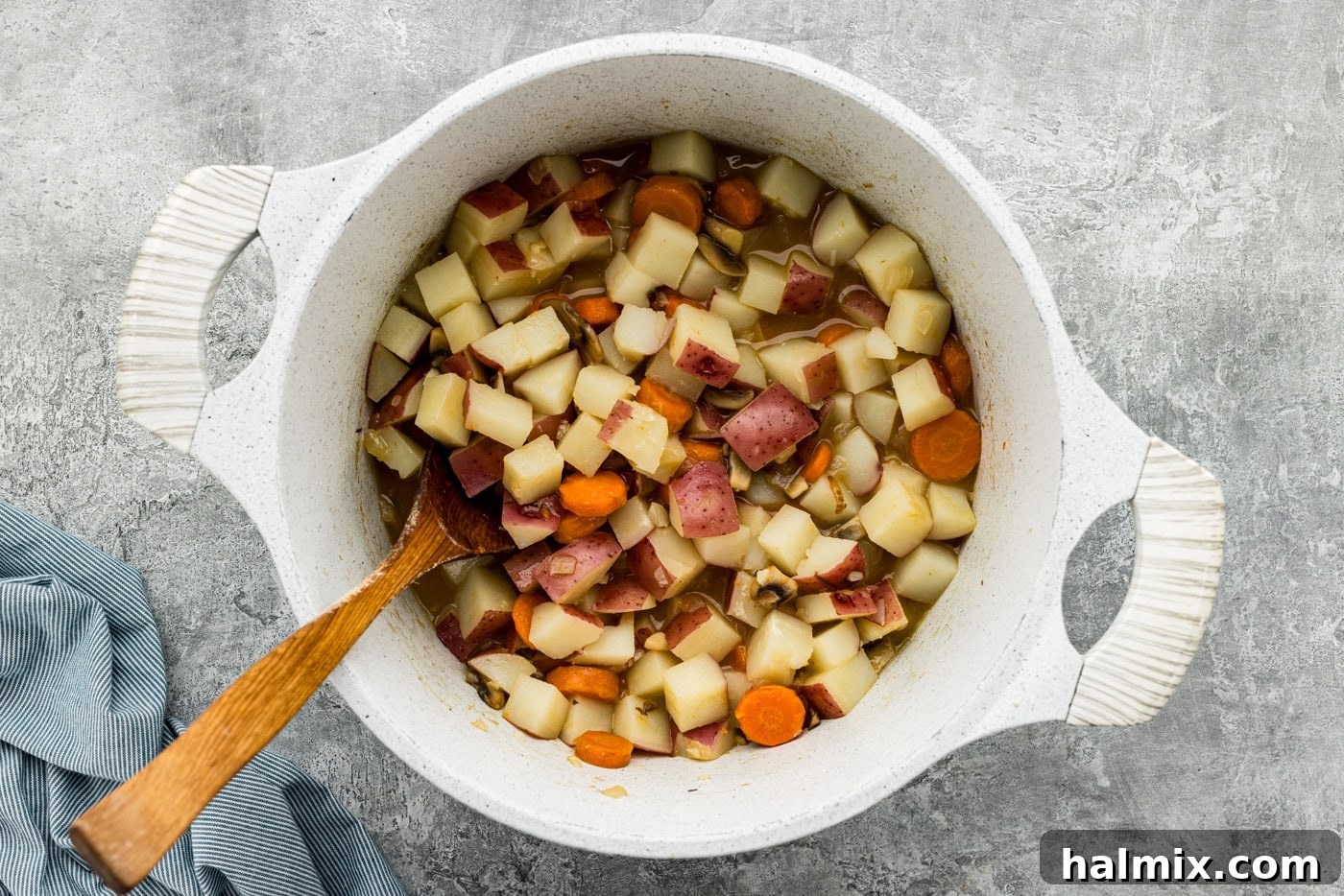 carrots, potatoes, mushrooms, and garlic in a Dutch oven with a wooden spoon