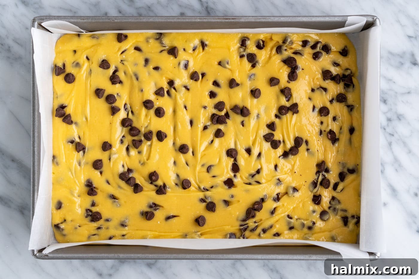 Reserved chocolate chips being sprinkled generously on top of the spread-out cake mix cookie bar batter before baking.