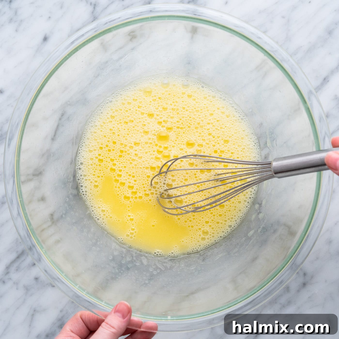 A hand whisking egg, water, and oil in a large mixing bowl to form the wet ingredients for the cookie bars.