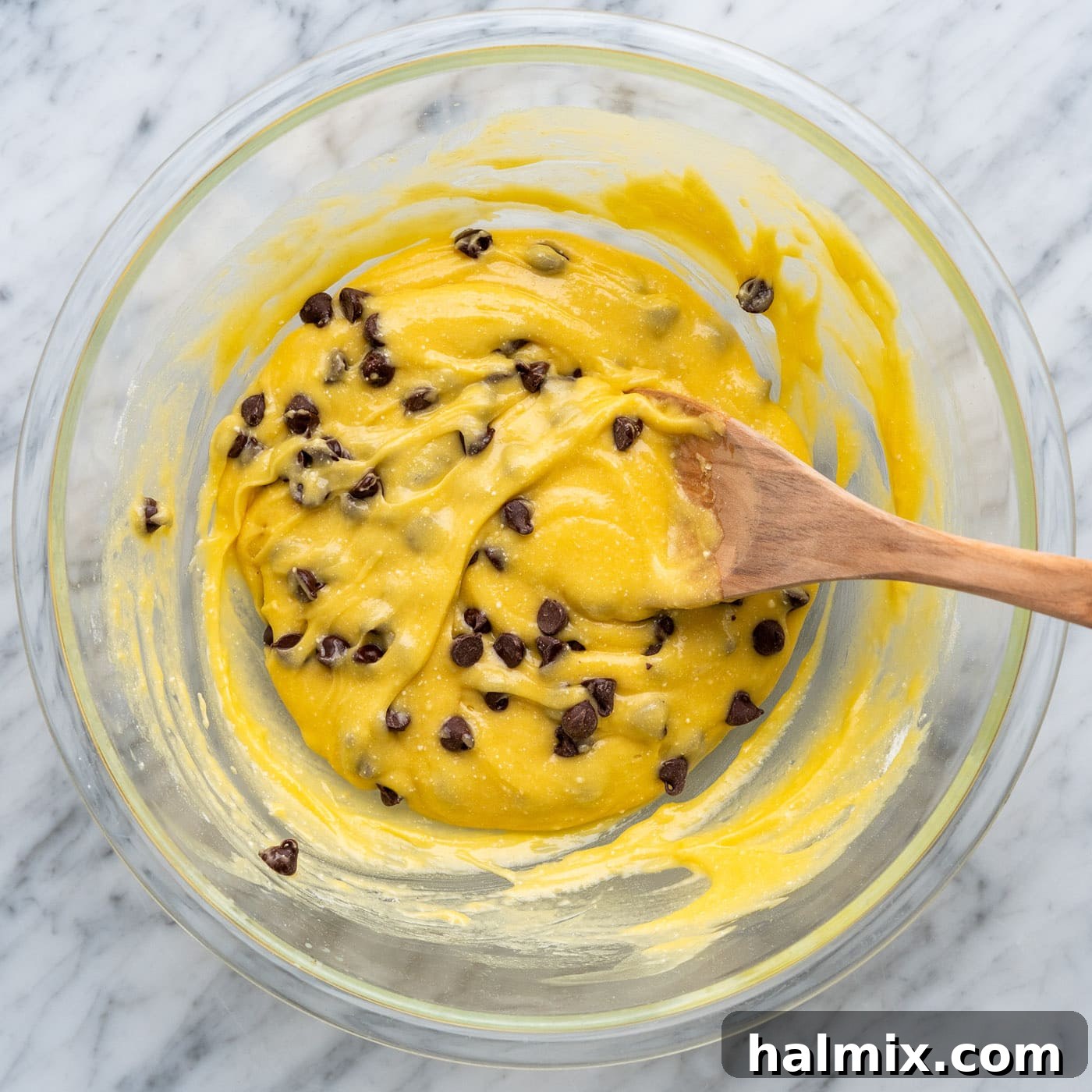 Cake mix cookie bar batter, mixed with chocolate chips, in a bowl with a wooden spoon.