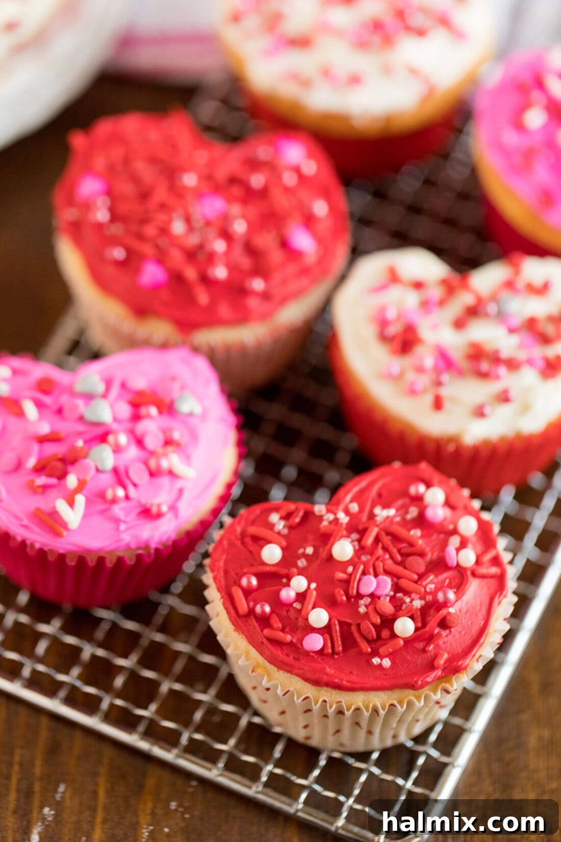 Heart shaped cupcakes on a cooling rack, adorned with white, pink, and red frosting.