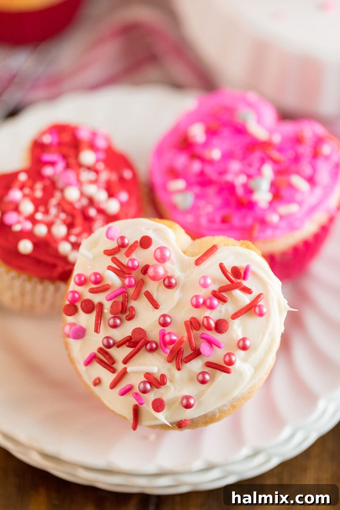 Three Valentine Heart Cupcakes on a white plate, frosted in pink and white with sprinkles.