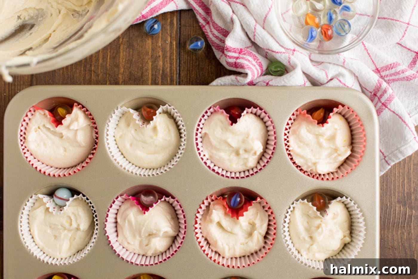 Cupcake batter in liners in a muffin pan with marbles to create heart shapes.