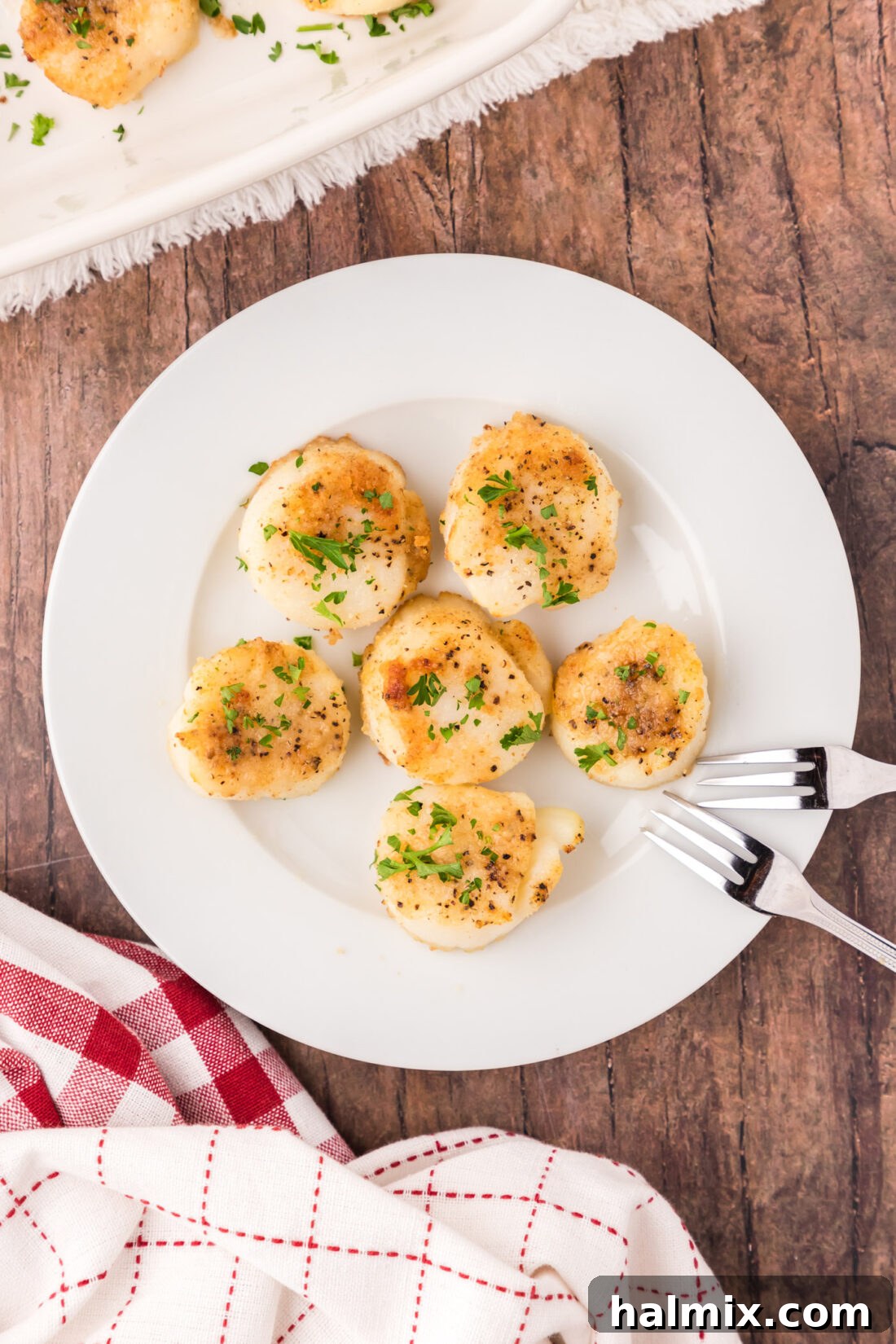 Lemon Garlic Baked Scallops 3 A plate featuring several golden-crusted baked scallops, garnished for serving.