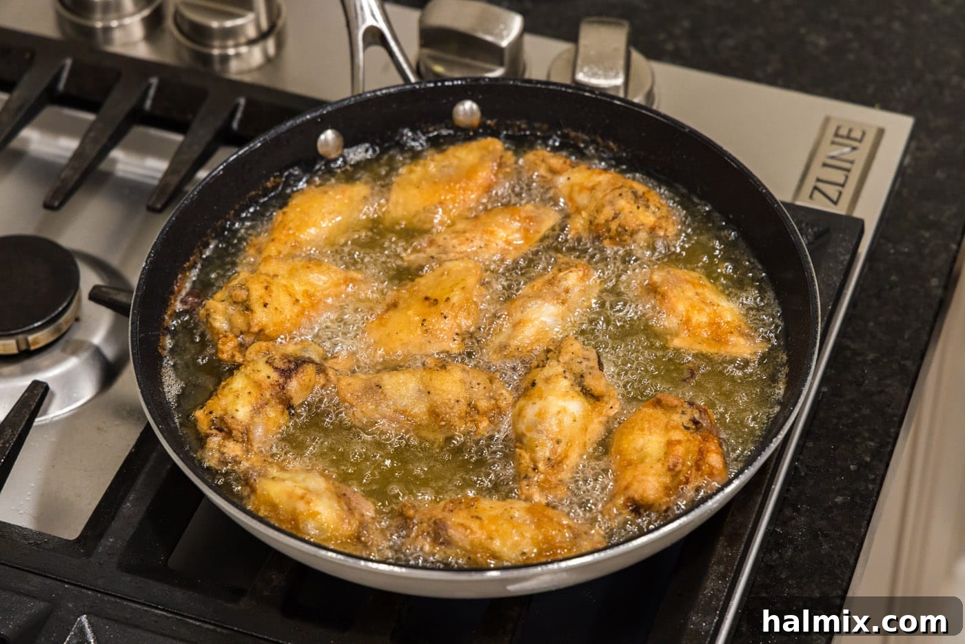 Fried chicken wings in a skillet of oil, almost ready to be removed.
