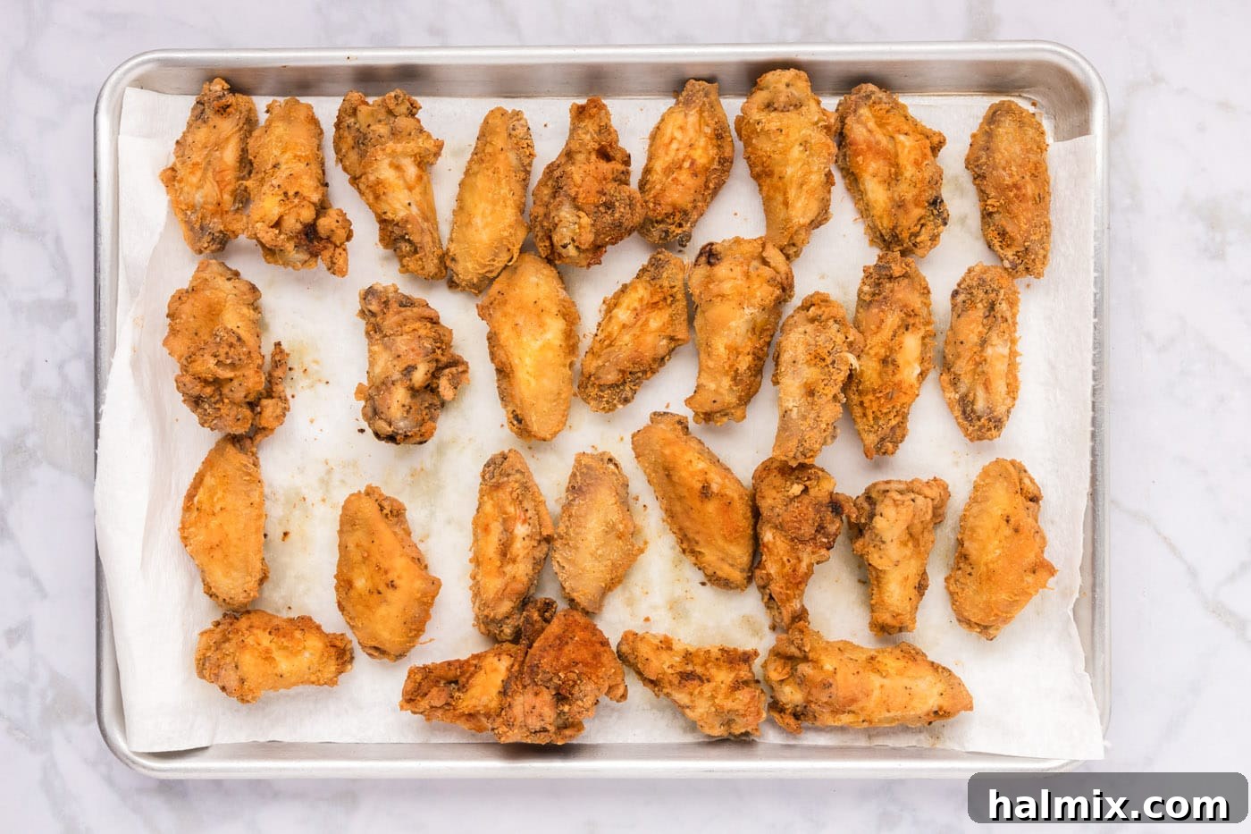 Fried chicken wings on a baking sheet lined with paper towels and a wire rack.