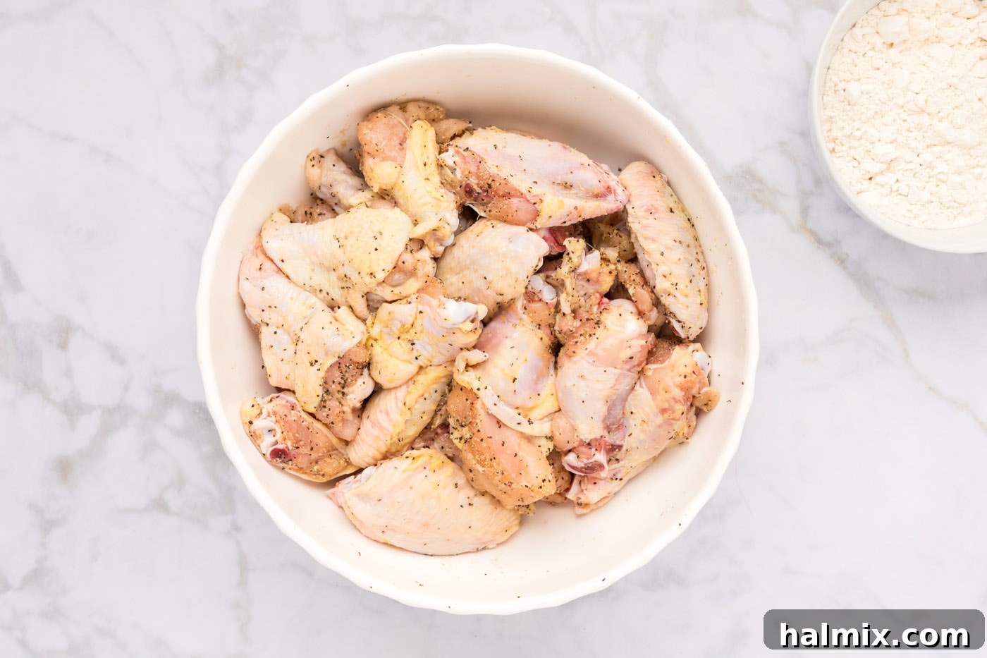 Seasoned chicken wings in a bowl, ready for flour coating.