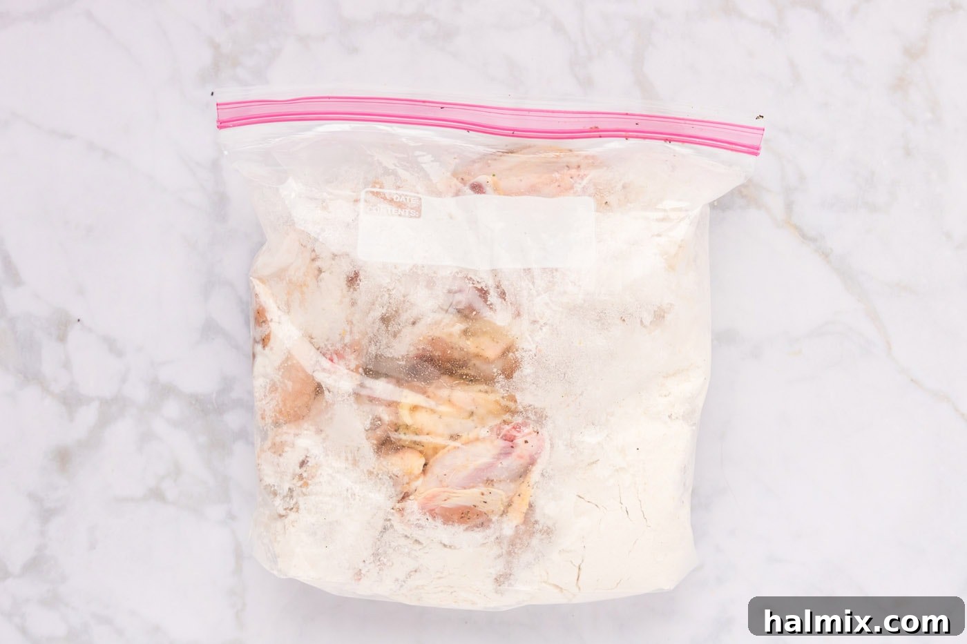 Chicken wings in a large zip-top bag with flour, being shaken to coat.