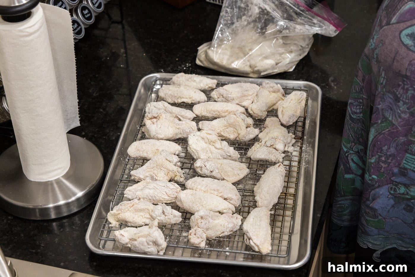 Floured chicken wings resting on a baking sheet with a wire rack.