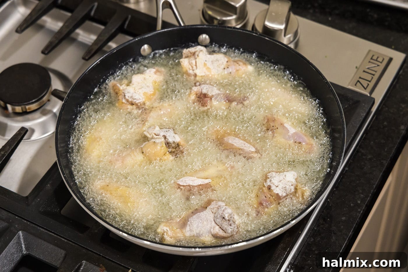 Chicken wings frying in a skillet of hot oil, bubbling nicely.