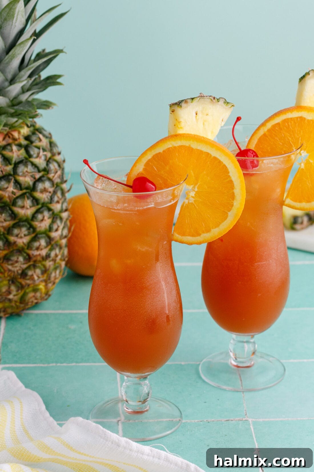 Two Rum Runners garnished with an orange wheel, pineapple wedge and cherry