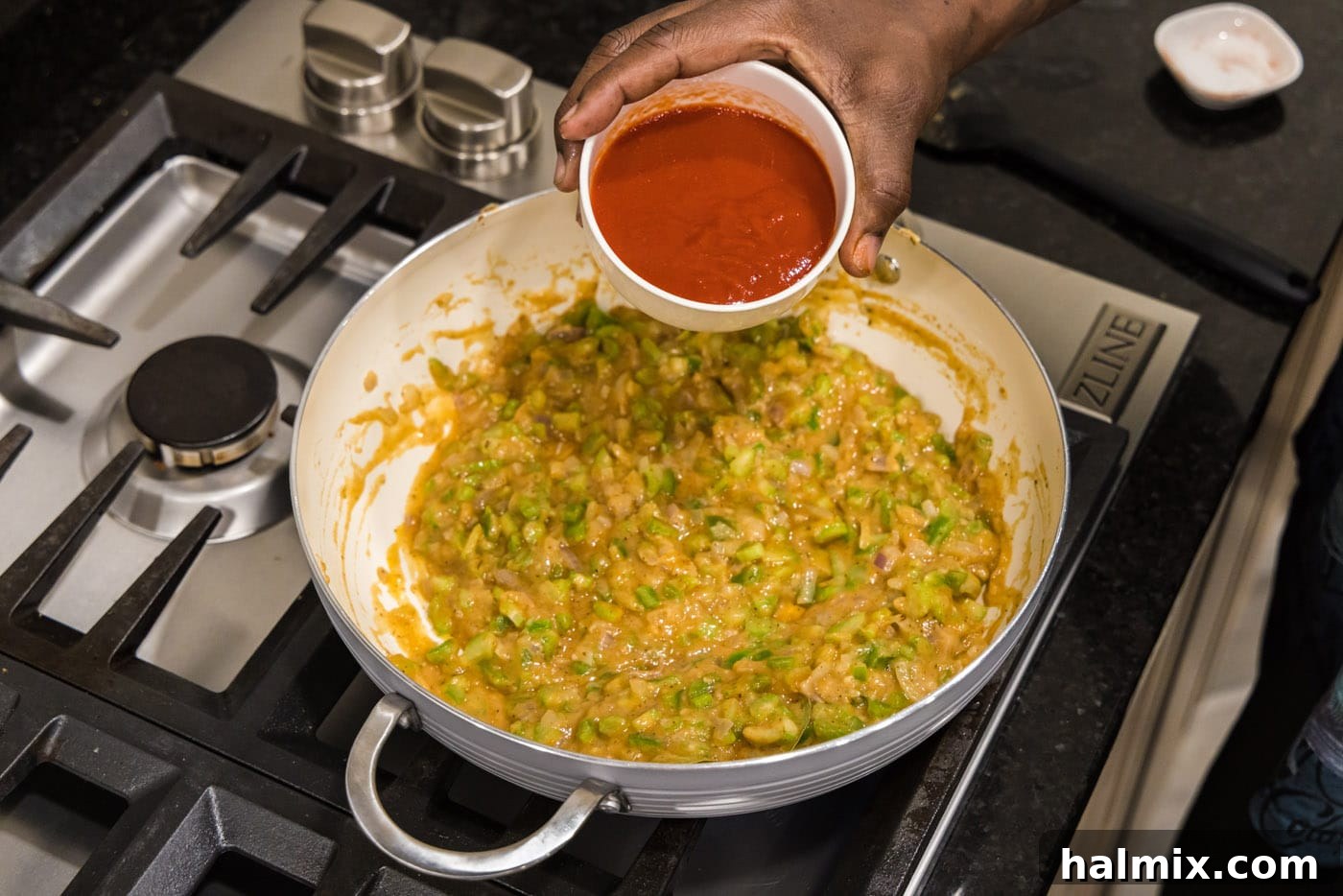 pouring tomato sauce into skillet with vegetable roux base
