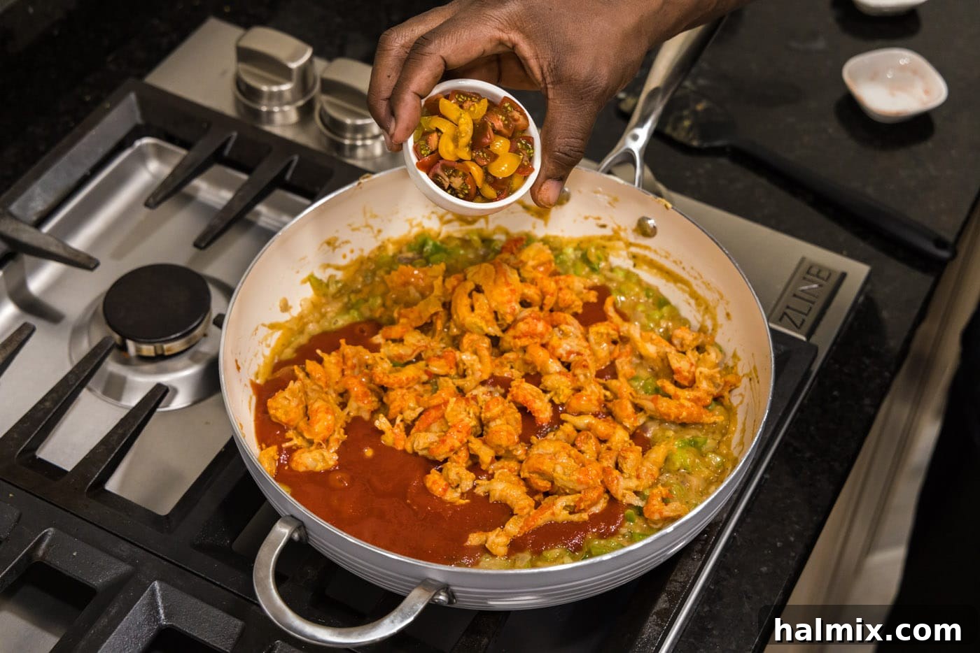 adding cherry tomatoes to crawfish etouffee in a skillet
