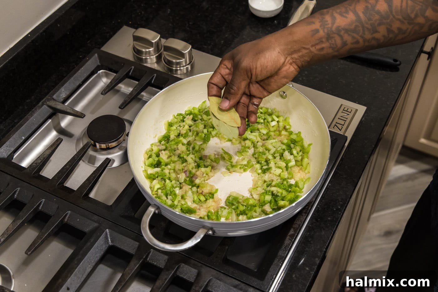 adding bay leaves to skillet of onion, bell pepper, and celery mixture