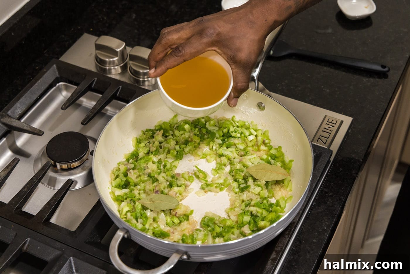 adding chicken stock to skillet of holy trinity vegetables and roux
