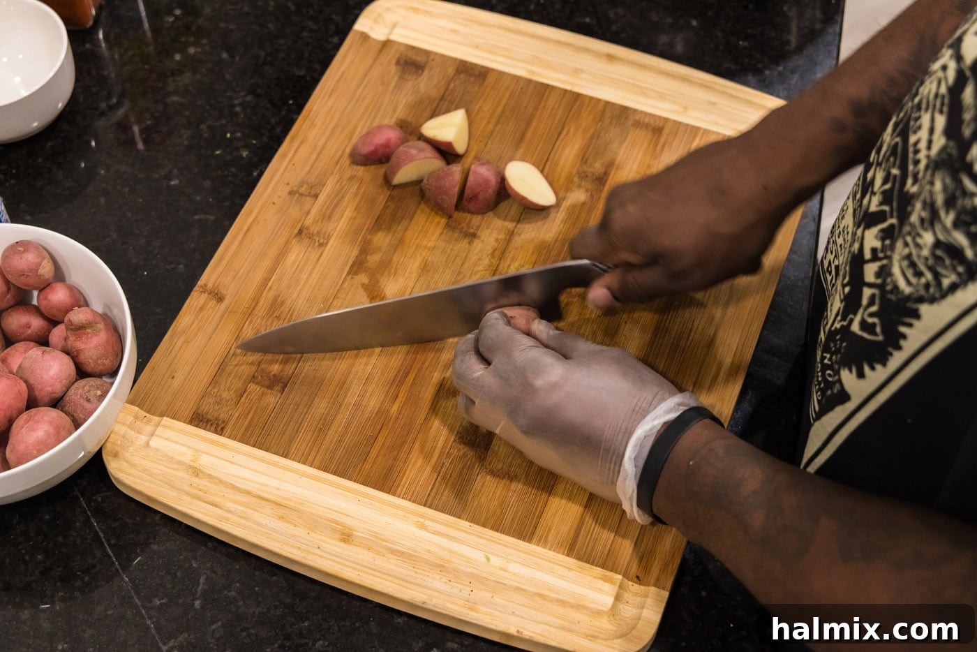 hands slicing baby red potatoes on a cutting board, ensuring even pieces