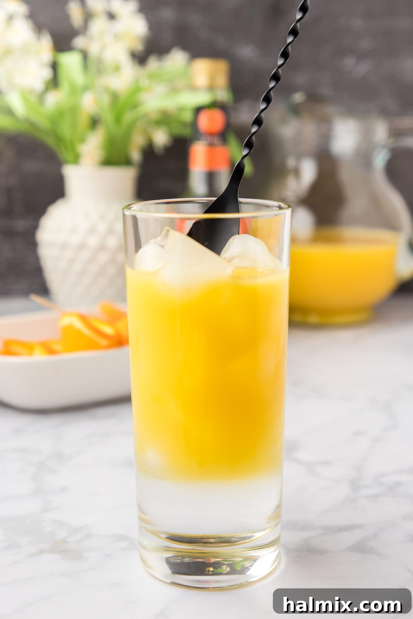 Velvet Peach Sunset 7 Mixing Fuzzy Navel cocktail in a glass with a cocktail spoon