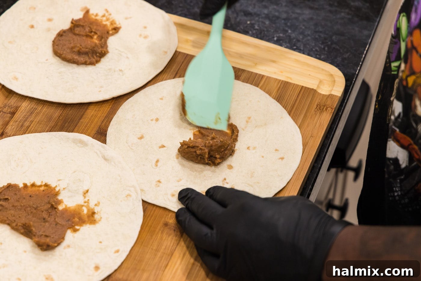 Deep-Fried Mexican Delights 11 spatula spreading refried beans onto taco shell, creating the base layer of the filling