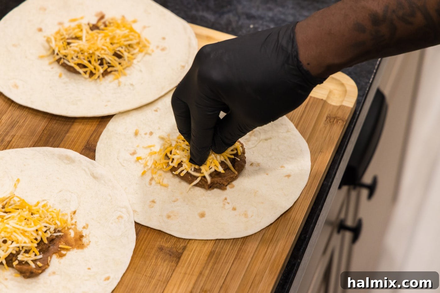 Deep-Fried Mexican Delights 12 adding shredded cheese on top of refried beans on a tortilla shell, preparing for the chicken mixture