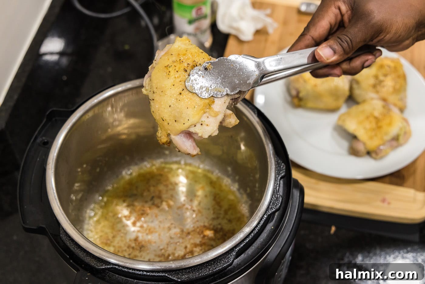 Seared chicken thighs being removed from the Instant Pot with tongs.