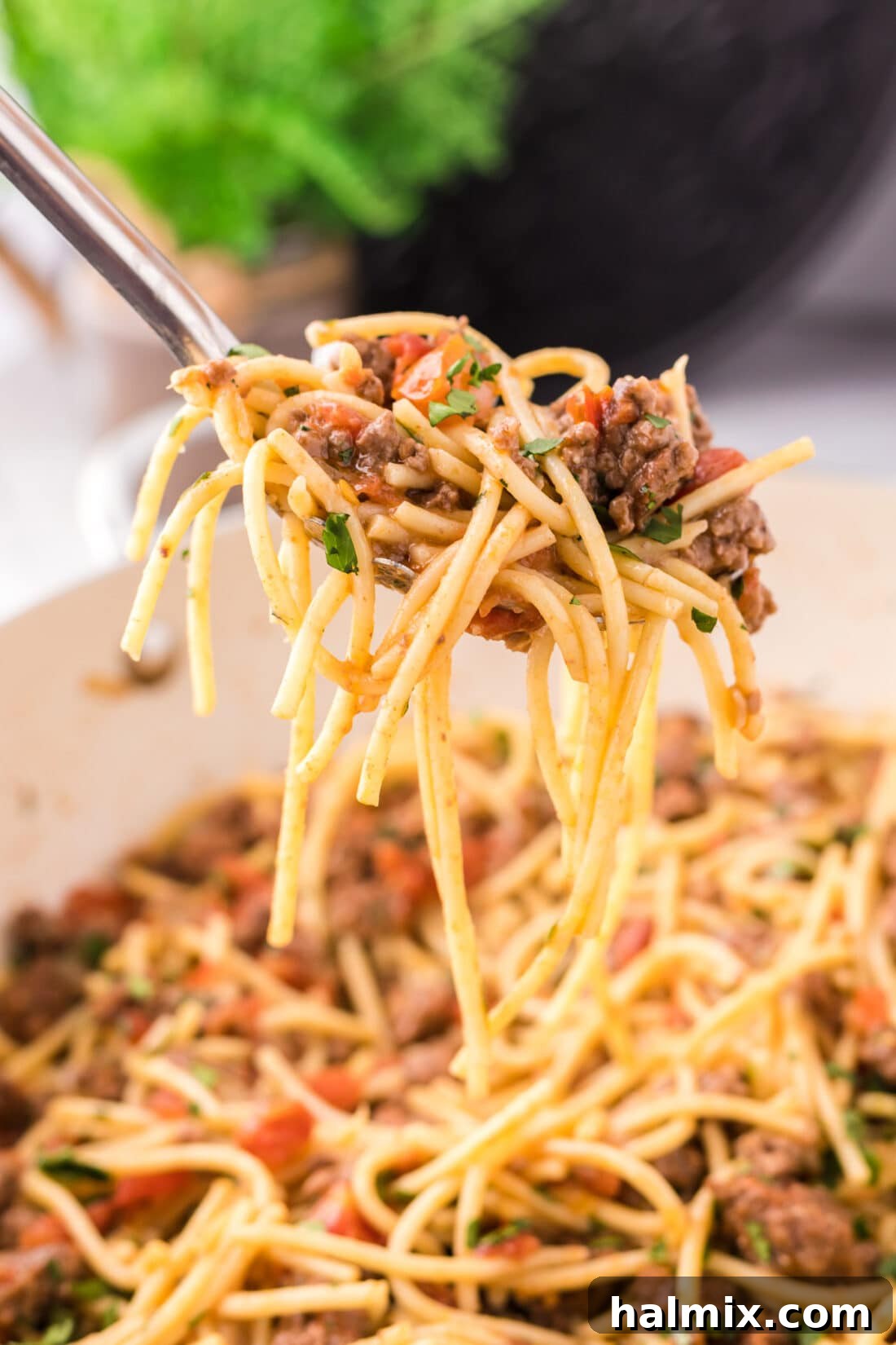 A spoon lifting a generous portion of cheesy Taco Spaghetti from a hot skillet, showcasing the rich texture and vibrant colors.