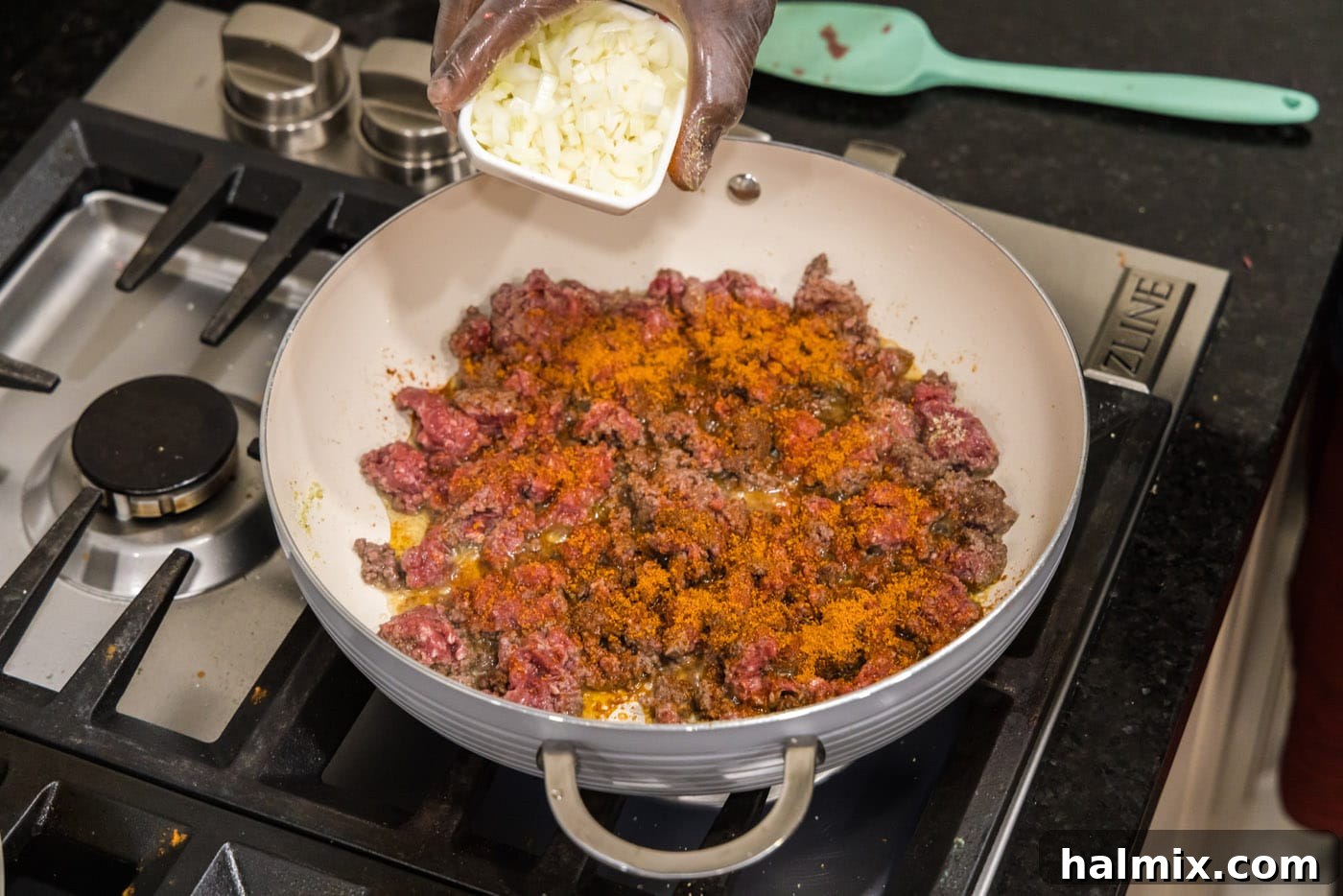 Adding finely chopped onion to a skillet with browning ground beef and taco seasoning, enhancing the flavor.