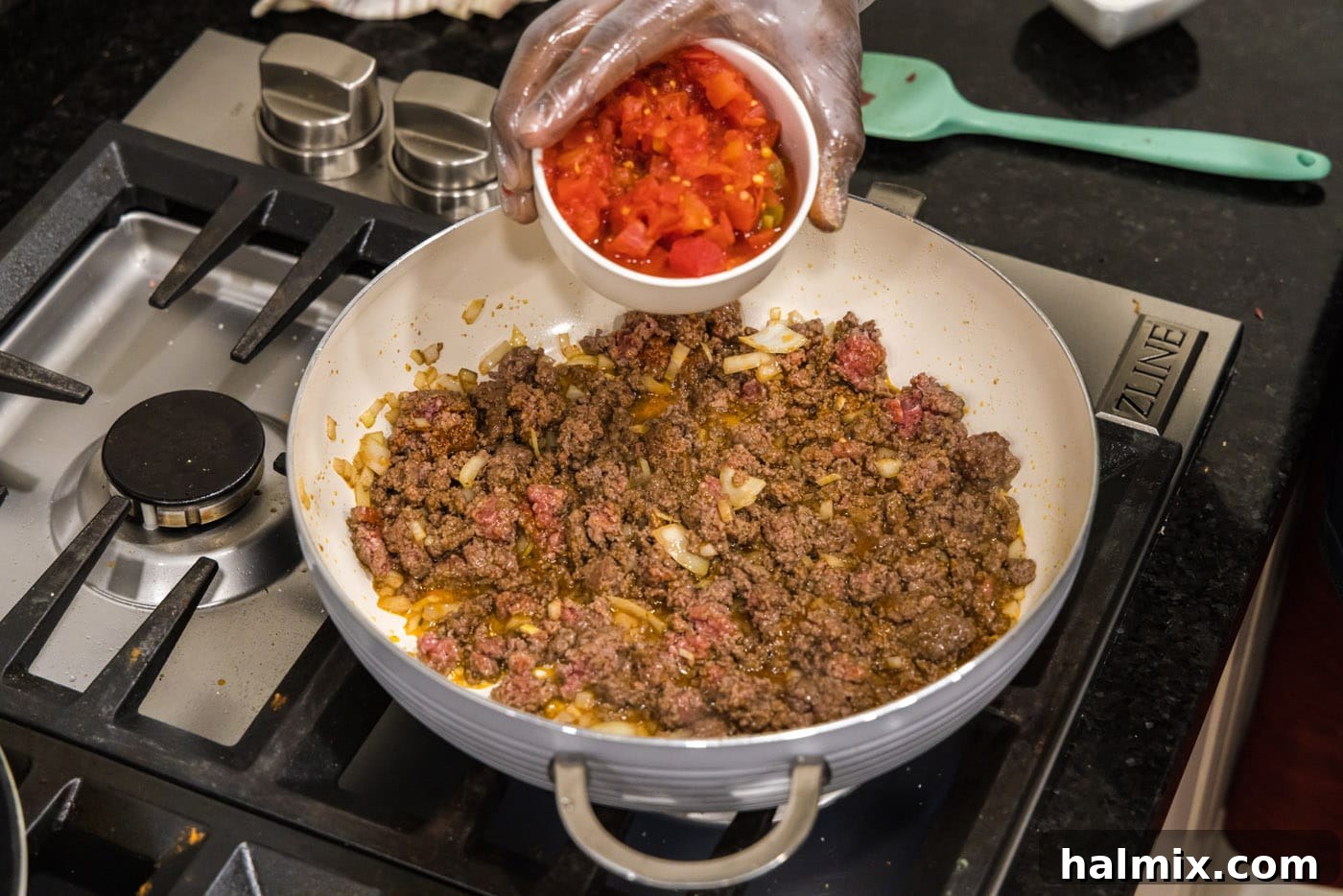 Adding a can of undrained Rotel tomatoes to the seasoned ground beef and onion mixture in the skillet, creating the sauce base.