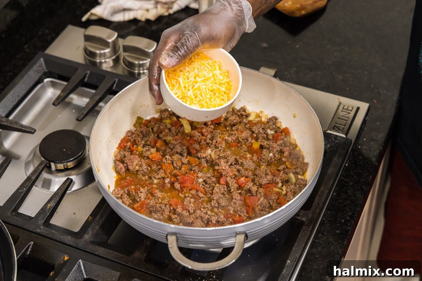 Sprinkling shredded cheddar cheese over the simmering ground beef, Rotel, and onion mixture, preparing for creamy goodness.