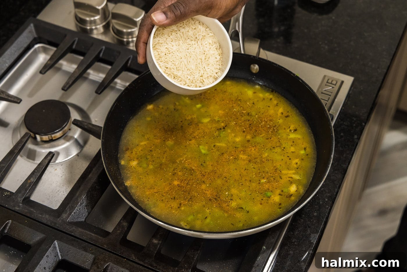 Spicy Southern Comfort Rice 9 Basmati rice being carefully poured into the skillet, joining the chicken stock and flavorful vegetables for simmering.