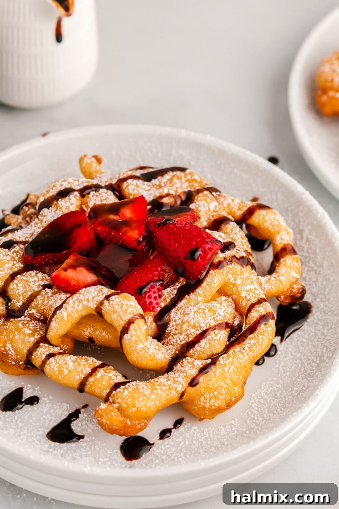 Golden Carnival Whirl 2 Close up photo of a Funnel Cake topped with chocolate sauce and strawberries, showcasing its crispy texture