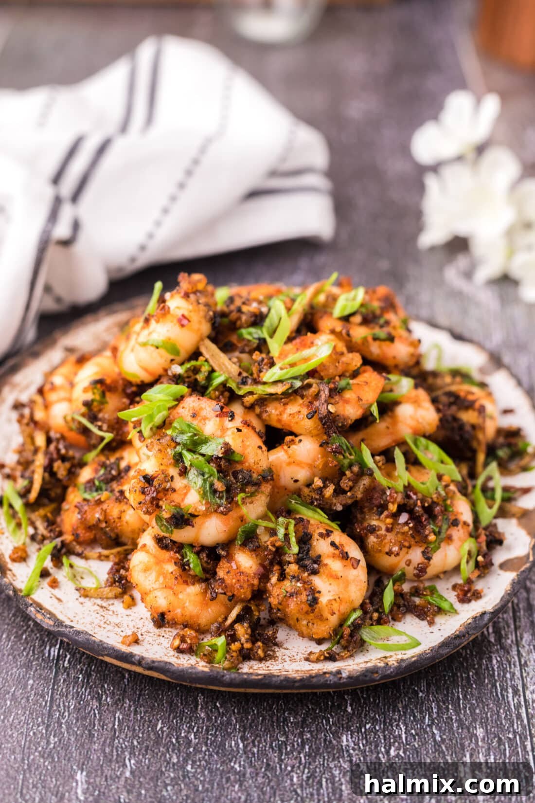 A beautifully arranged plate of golden-brown crispy salt and pepper shrimp, garnished with green onions and chili flakes.