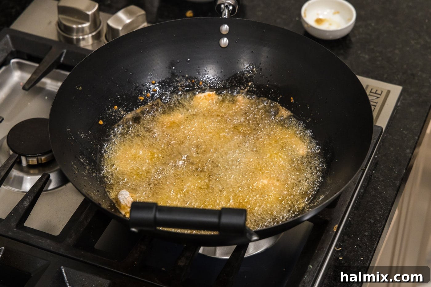 Coated shrimp being carefully placed into hot oil in a wok, frying to a golden crisp.