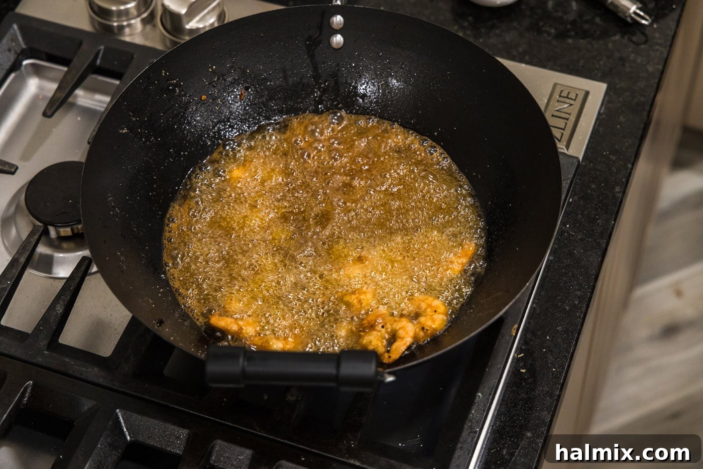 Batch of perfectly fried, golden-brown shrimp sizzling in the hot oil within a wok.