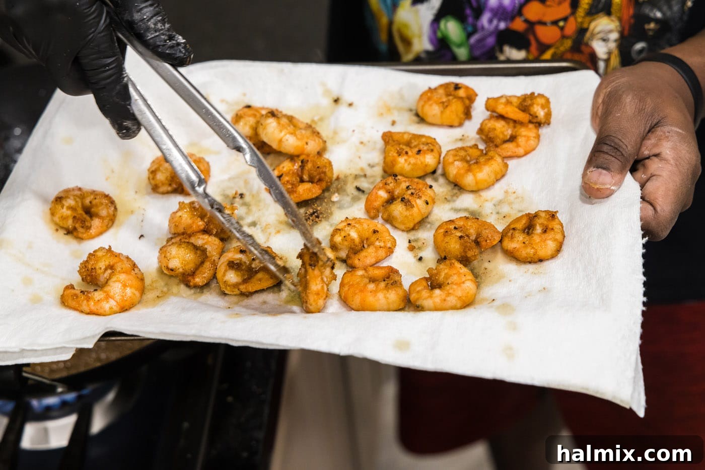 Using tongs to transfer crispy fried shrimp from the wok to a paper towel-lined plate for draining.
