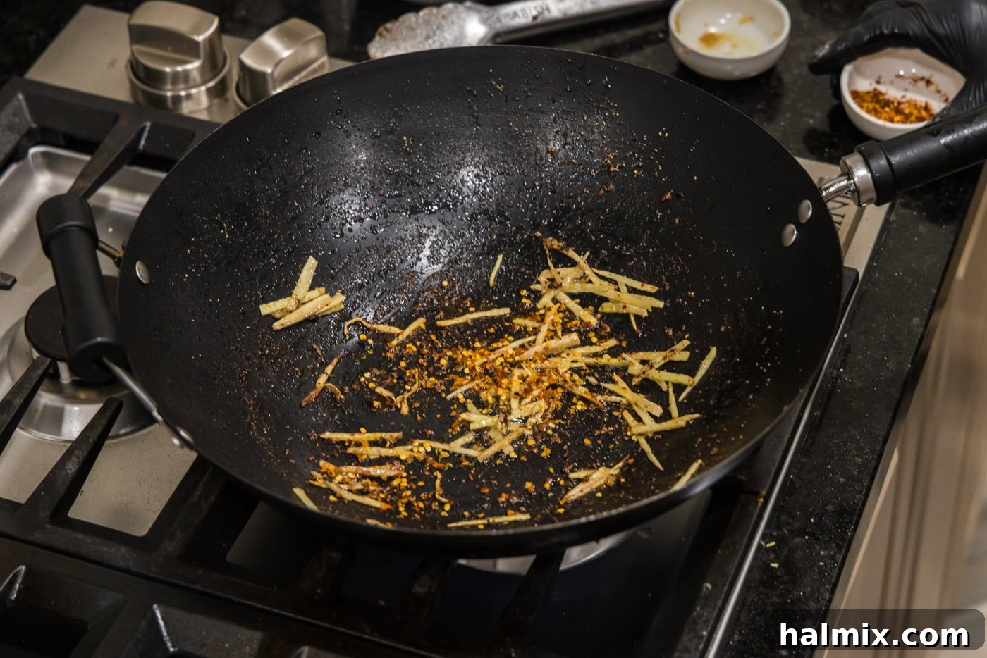 Red pepper flakes added to the wok with slivered ginger, stirring to combine the aromatics.