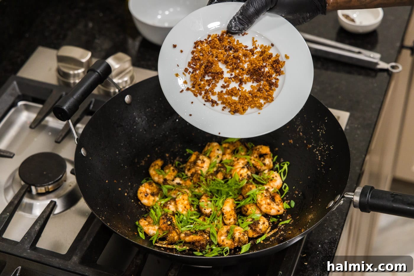 Adding crispy fried garlic to the salt and pepper shrimp in the wok, along with green onions and other seasonings.