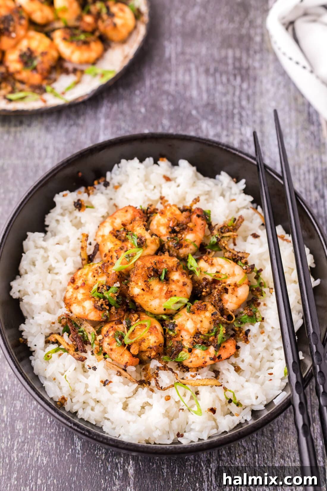 A bowl of crispy salt and pepper shrimp served over a bed of fluffy white rice, garnished with fresh green onions.